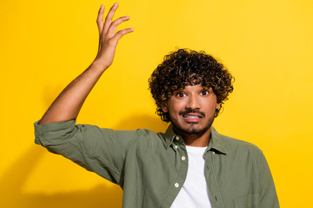 Portrait photo of young hispanic guy in khaki shirt confused raised hand questioned stupor isolated on yellow color backgroundの写真素材