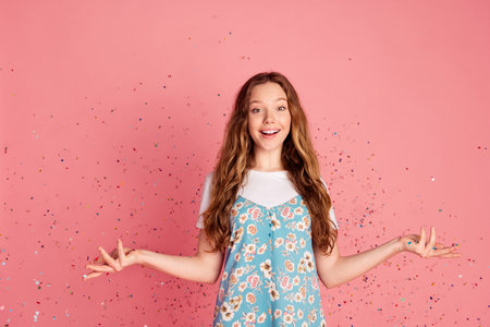 Portrait of lovely young girl flying confetti wear dress isolated on pink color background