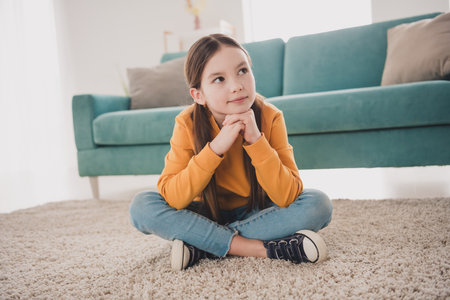 Full size photo of cute little girl wear sweater sitting floor fantasize living room apartment indoorsの写真素材