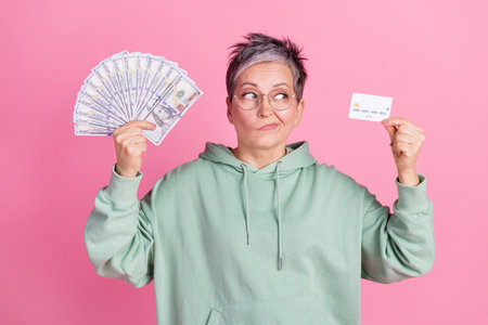 Photo of doubtful unsure lady dressed khaki sweatshirt holding money fan credit card isolated pink...
