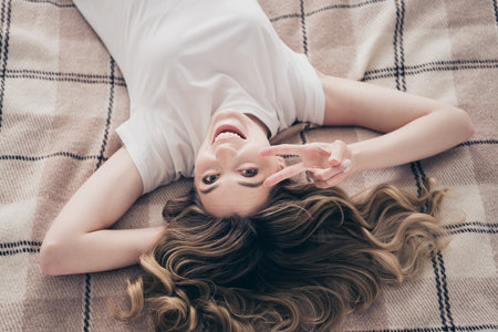 Top view photo of positive girl lying bed make v sign in comfort room indoorsの写真素材