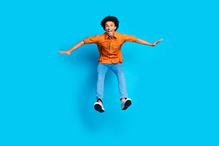 Full length photo of impressed positive guy dressed orange shirt jumping high empty space isolated...