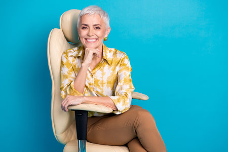 Photo portrait of lovely pensioner lady sit armchair charming dressed stylish elegant garment isolated on blue color backgroundの写真素材