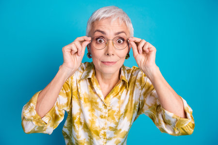 Photo portrait of lovely pensioner lady amazed touch eyewear dressed stylish elegant garment isolated on blue color backgroundの写真素材