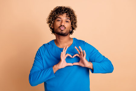 Photo of nice funny guy wear trendy blue clothes heart sign isolated on beige color backgroundの写真素材