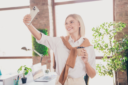 Photo of attractive young woman selfie photo hold coffee dressed trendy clothes executive business leader comfort beautiful office interiorの写真素材