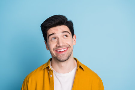 Photo of cheerful positive guy dressed yellow shirt looking emtpy space isolated blue color...