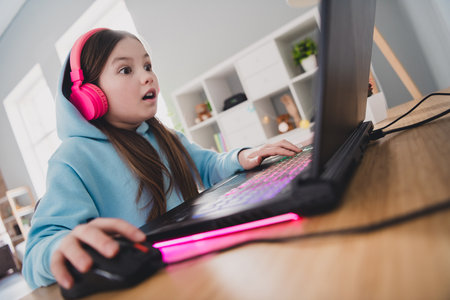 Photo of astonished crazy adorable girl little gamer online video computer game competition indoors houseの写真素材