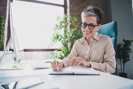 Photo of attractive good mood age lady agent dressed formal shirt writing textbook indoors workplace workstation loftの写真素材