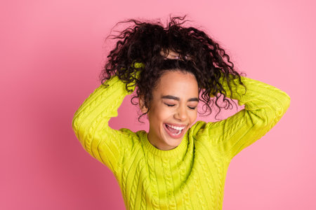 Portrait photo of youth model teenager girl promoting new trend hair trying to make bun and laughing isolated on pink color backgroundの写真素材