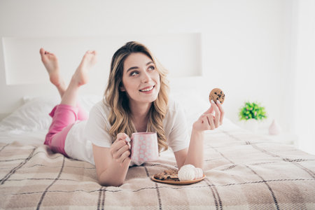 Photo of positive girl lying bed eating tasty yummy breakfast with cacao in bedroomの写真素材