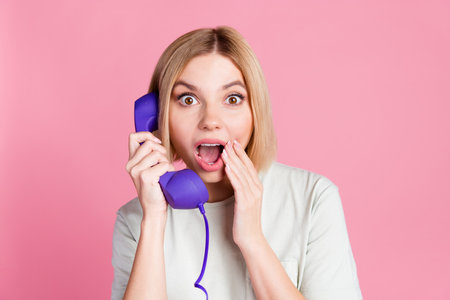 Portrait of ecstatic impressed girl with bob hair wear t-shirt discuss rumors on retro cable phone isolated on pink color backgroundの写真素材
