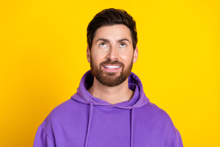Portrait of positive cheerful man with stylish bristle dressed purple hoodie look at promo empty space isolated on yellow color backgroundの写真素材