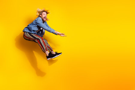 Full size photo of pretty young guy jumping pushing invisible things wear trendy jeans outfit isolated on yellow color backgroundの写真素材