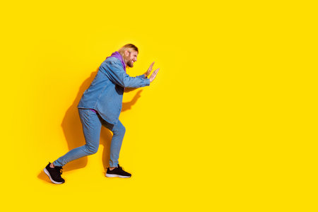 Full length profile portrait of nice young man push empty space wear denim jacket isolated on yellow color backgroundの写真素材