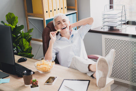 Photo of attractive good mood age lady recruiter dressed formal shirt enjoying potato chips indoors workplace workstationの写真素材