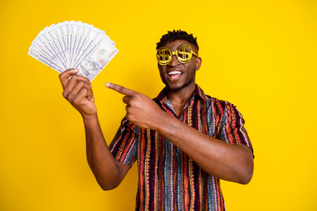 Portrait of nice young man point finger money wear shirt isolated on yellow color backgroundの写真素材