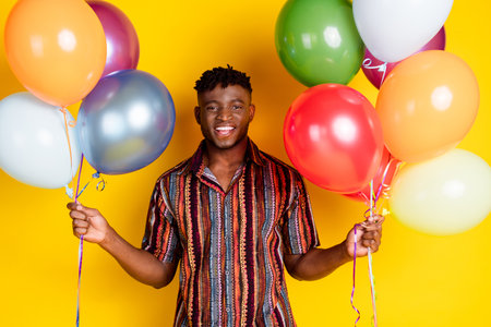 Photo of nice young man hold balloons wear shirt isolated on yellow color backgroundの写真素材