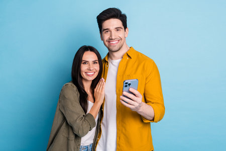 Portrait of two young people cuddle smart phone wear shirt isolated on blue color background