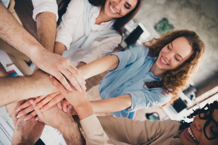 Cropped portrait of group professional corporate workers pile stack hand shake loft interior business center indoorsの写真素材