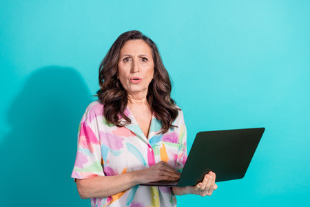 Photo portrait of attractive senior woman nervous hold netbook dressed stylish colorful clothes isolated on cyan color backgroundの写真素材