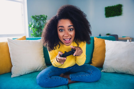 Photo of cheerful positive girl sitting on sofa playing video game cosy flat living room daylight...