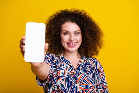 Photo portrait of pretty young girl show white screen device wear trendy colorful outfit isolated on yellow color backgroundの写真素材