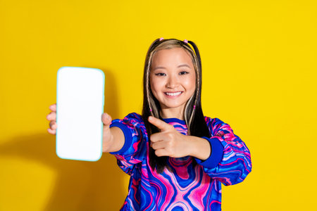 Portrait of clever woman with dyed hair directing at ui design on smartphone display empty space isolated on yellow color backgroundの写真素材