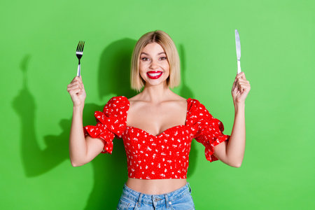 Photo of positive excited girl hold fork knife smiling isolated green color backgroundの写真素材
