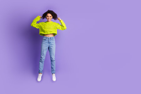 Full body photo of attractive young woman jump show biceps dressed stylish green clothes isolated on violet color backgroundの写真素材