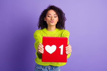 Photo of young wavy haired kissing girl in green pullover holding red like button dating network...