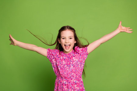 Portrait of lovely schoolgirl arms throw hair wear pink dress isolated on green color background