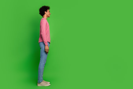 Full length photo of attractive funny guy wear pink sweater smiling looking emtpy space isolated green color backgroundの写真素材