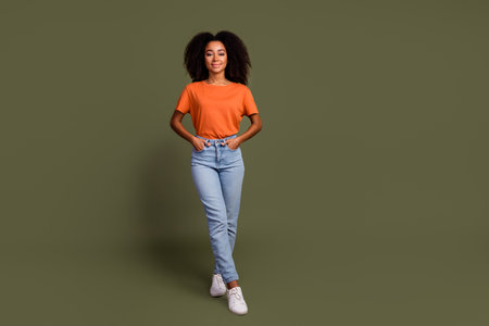 Full size photo of lovely pleasant girl wear orange t-shirt denim pants holding palms in pockets...