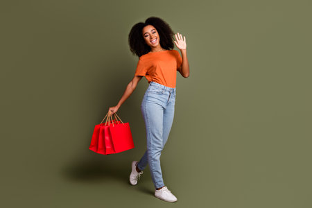 Full length photo of shiny attractive lady dressed orange outfit holding bargains waving hi empty...