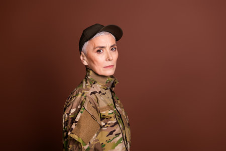 Photo of strong serious elderly lady dressed camo uniform support country empty space isolated brown color backgroundの写真素材