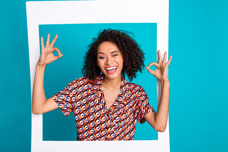 Photo of attractive girl in photo frame wink make okay sign isolated blue cyan color backgroundの写真素材