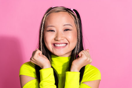 Photo of optimistic excited chinese girl with dyed hairdo dressed yellow turtleneck clenching fists...