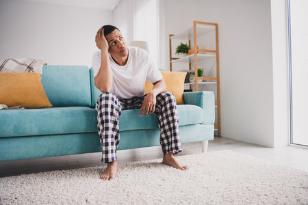 Photo of unhappy upset guy sleepwear pajama smiling stayinh home sofa feeling bad indoors house apartment roomの写真素材