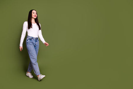 Full length photo of lovely young lady walking empty space dressed stylish white garment isolated on khaki color backgroundの写真素材