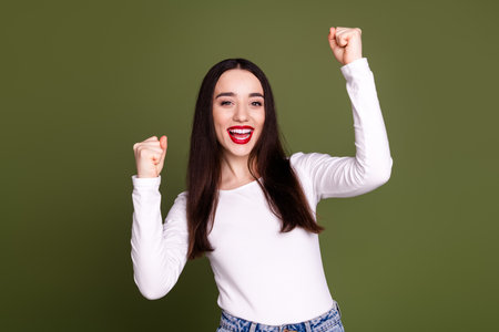 Photo portrait of pretty young girl winning raise fists wear trendy white outfit isolated on khaki color backgroundの写真素材