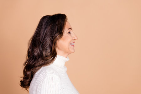 Profile photo of lovely cheerful woman wear white stylish clothes look empty space isolated on beige color backgroundの写真素材