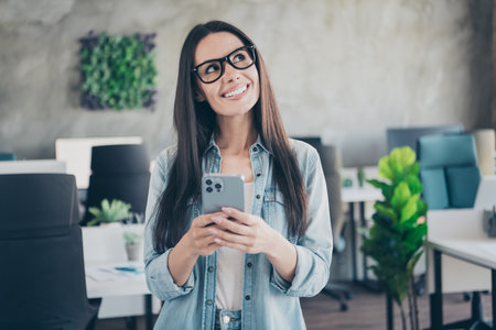 Photo of dreamy good mood lady agent dressed jeans shirt chatting modern device indoors workplace workstation loftの写真素材