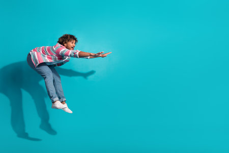 Photo of positive crazy man wear trendy striped clothes fly air empty space isolated on cyan color...