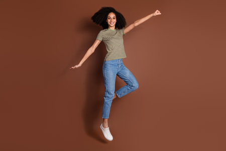 Full length photo of charming positive girl wear striped t-shirt jumping high hurrying empty space...