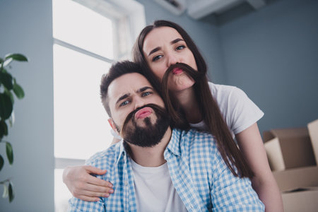 Photo of two young partners hair pretend mustache relocating moving box package new modern flat indoorsの写真素材