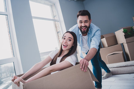 Photo of two young partners rejoice push sit package box relocating moving new modern flat indoors