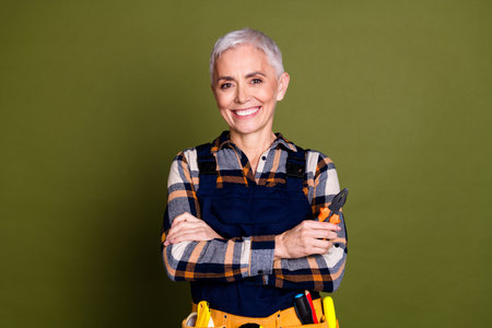 Photo of pretty senior female professional expert handyman crossed hands wear blue workwear overall isolated on khaki color backgroundの写真素材