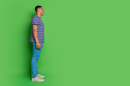 Photo of cheerful young nice man wear striped stylish clothes outfit look empty space isolated on green color backgroundの写真素材