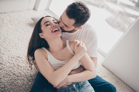 Photo of attractive trendy cheerful married young couple spending free time lying floor kiss cheek...